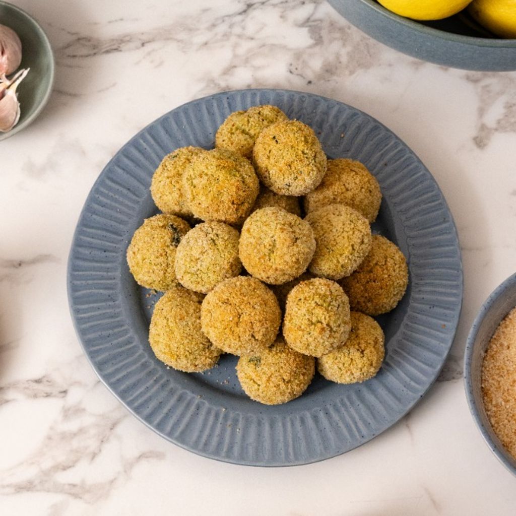 Homemade cod and zucchini meatballs on a serving plate with fresh zucchini, lemon and breadcrumbs, ready to cook.