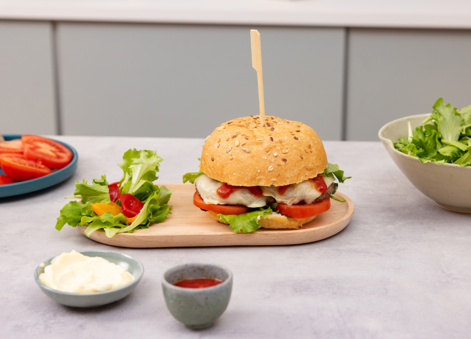 Hamburger con semi di sesamo con lattuga, pomodoro e salsa cremosa, servito nel panino con ingredienti di accompagnamento.