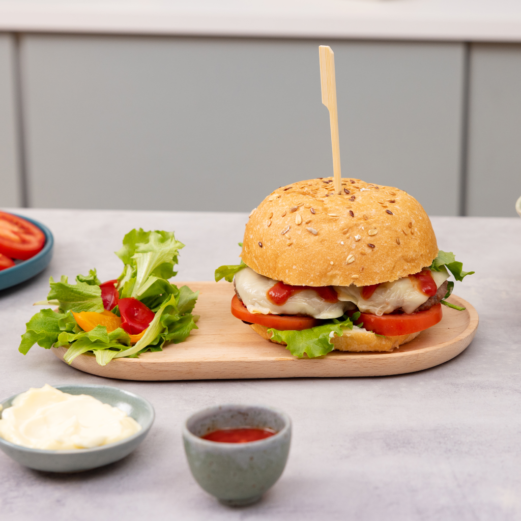 Hamburger con semi di sesamo con lattuga, pomodoro e salsa cremosa, servito nel panino con ingredienti di accompagnamento.