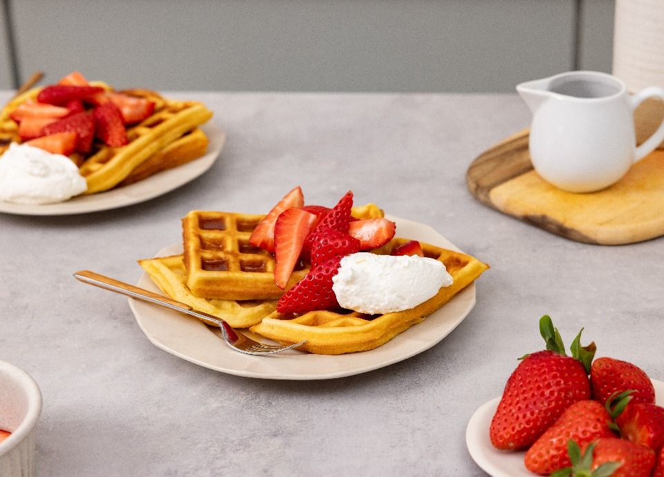 Waffle dorati guarniti con fragole fresche e panna montata su un piatto.
