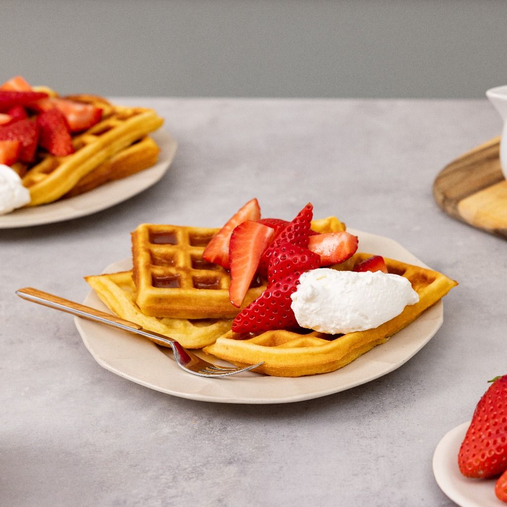 Waffle dorati guarniti con fragole fresche e panna montata su un piatto.