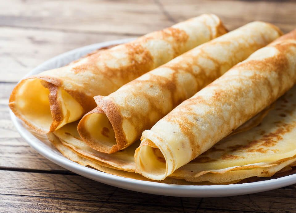 Rolled thin crepes arranged on a white plate over a wooden table.