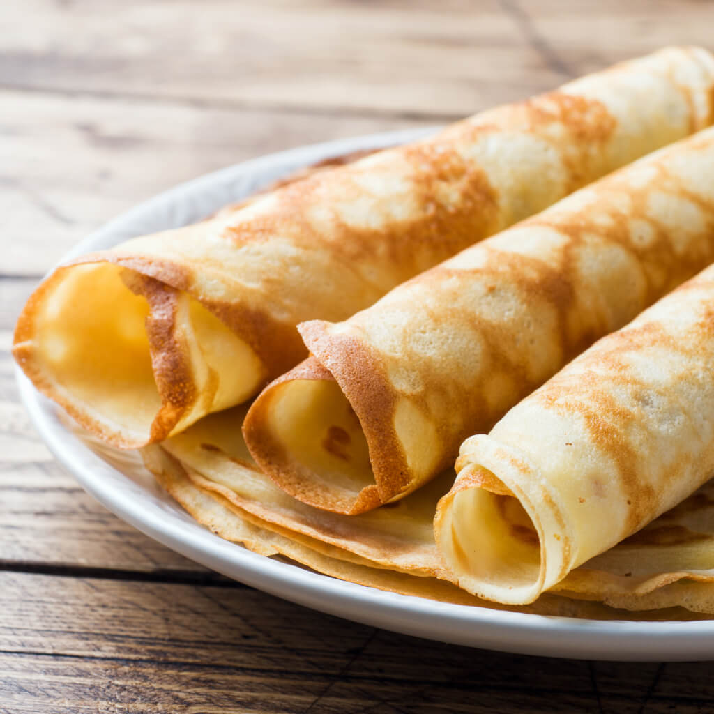 Rolled thin crepes arranged on a white plate over a wooden table.