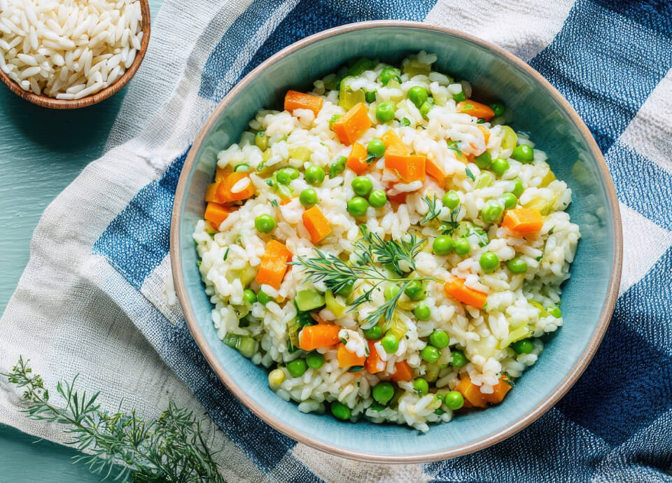 Risotto alle verdure con piselli, carote e zucchine servito in una ciotola su tovaglietta a quadri.