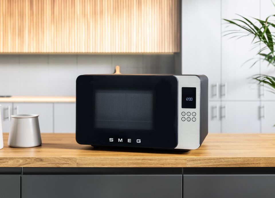 Black MOC01 Microwave on a wooden kitchen countertop, with light wood cabinets and grey walls in the background.