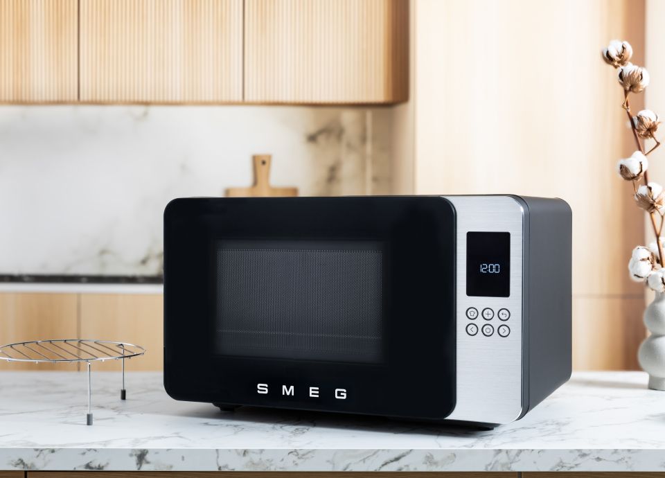 Black MOC01 Microwave on a marble kitchen countertop, with an accessory beside it and wooden cabinets and a marble wall in the background.
