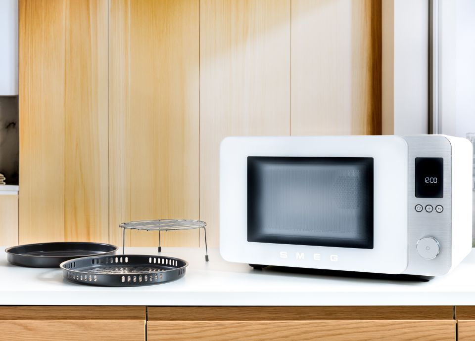 White MOC02 Microwave on a white kitchen countertop, with accessories beside it and wooden cabinets in the background.