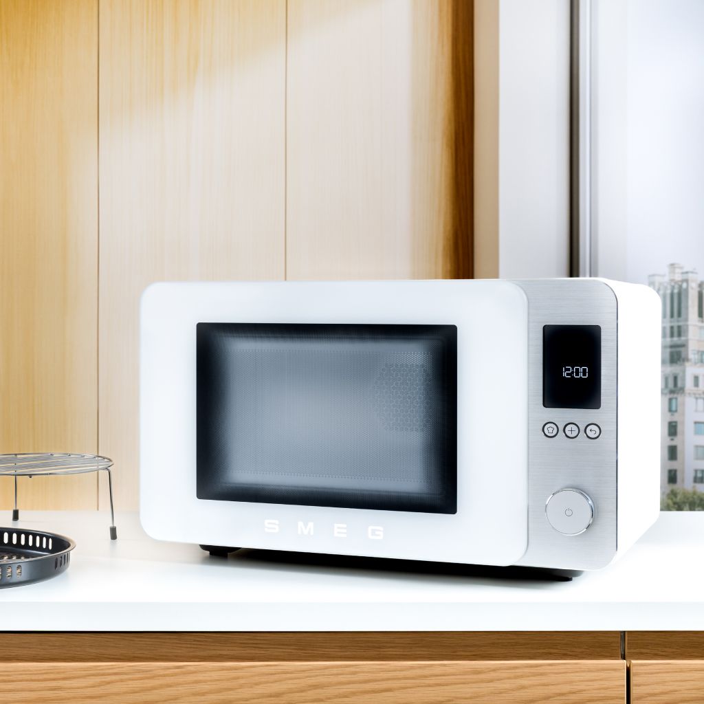 Forno microondas combinado Smeg em branco, com comandos digitais, colocado sobre uma bancada de cozinha contemporânea.
