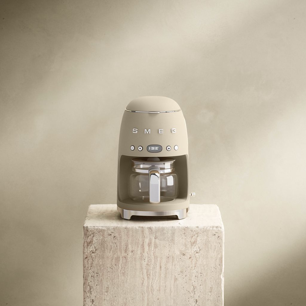 A Moonlight Smeg 50s style filter coffee machine with a glass carafe sits on a stone plinth against a soft neutral background.