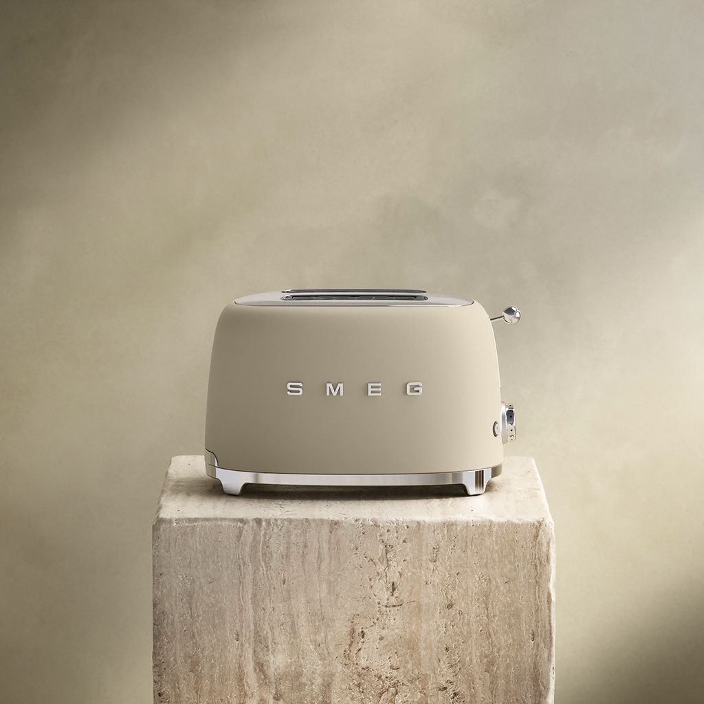 A Moonlight Smeg 50s Style 2-slice toaster with chrome accents sits on a textured stone block against a neutral wall
