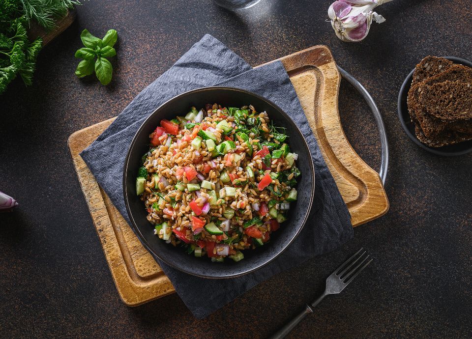 A dish of delicious looking food including  rice, chopped cucumber, tomatoes, onions, radishes and more, ready to be enjoyed!